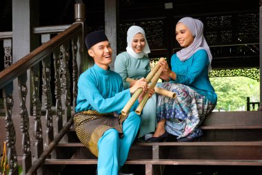 Geleneksel kostümlü üç Malaylı Müslüman 'dan oluşan bir grup geleneksel ahşap evin terasında Aidilfitri kutlaması sırasında mutlu bir konuşma yapıyorlar. Raya ve Müslüman moda konsepti.