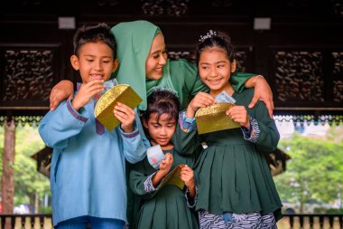 Mutlu ve heyecanlı çocuklar, bayram kutlamalarında annelerinden bir zarf dolusu harçlık ya da raya angpao taşıyorlar. Malezya Ailesi ve Raya Kavramı.