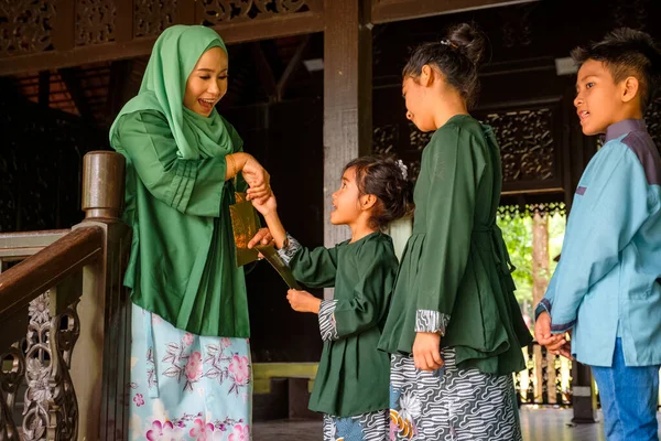 Mutlu anne bayram kutlaması sırasında çocuklarına harçlık ya da raya angpao zarfı veriyor. Malezya Ailesi ve Raya Kavramı.