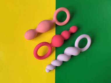 Anal tıkaçlar, kıç tıkaçları. Üç seks oyuncağı. Anal oyuncaklar. Sarı ve yeşil arka plan. Seks dükkanı için kullanışlı. 