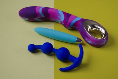 Vibratörler ve anal tıkaç. Sarı arka planda üç seks oyuncağı. Seks dükkanı ya da yetişkinler için kullanışlı