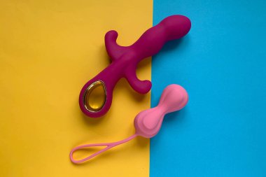 Seks oyuncakları. Pembe vibratör ve sarı-mavi arka planda sallanan toplar. Yetişkin için kullanışlı