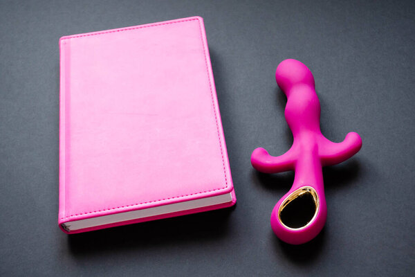 Sex toy. Pink vibrator and notepad on a black background. Useful for adult