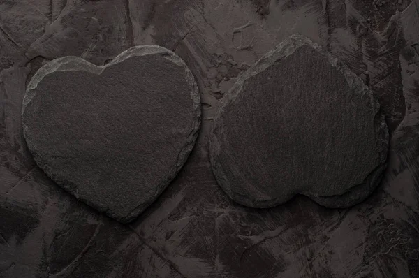 Two coasters made of black slate in the shape of a heart on a dark stucco background. Copy space — Stock Photo, Image