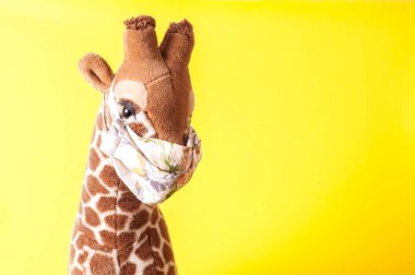 Sarı arka planda maske takmış oyuncak zürafa. Coronavirüs