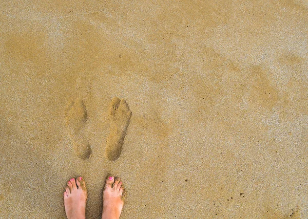 在潮湿的黄沙上，赤脚女人的脚在她们自己的指纹旁边有一个红色的脚趾头 — 图库照片