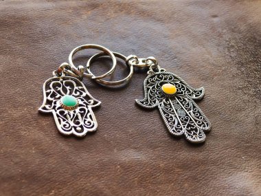 Kahverengi deri arka planda Fatima Hand şeklinde iki anahtarlık. Eski bir sembol ve geleneksel Tunus turist hatırası.