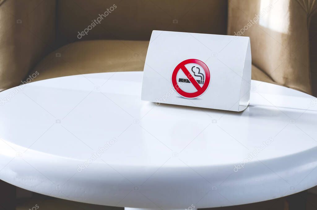 White cardboard sign No smoking on a white round table. Hotel interior