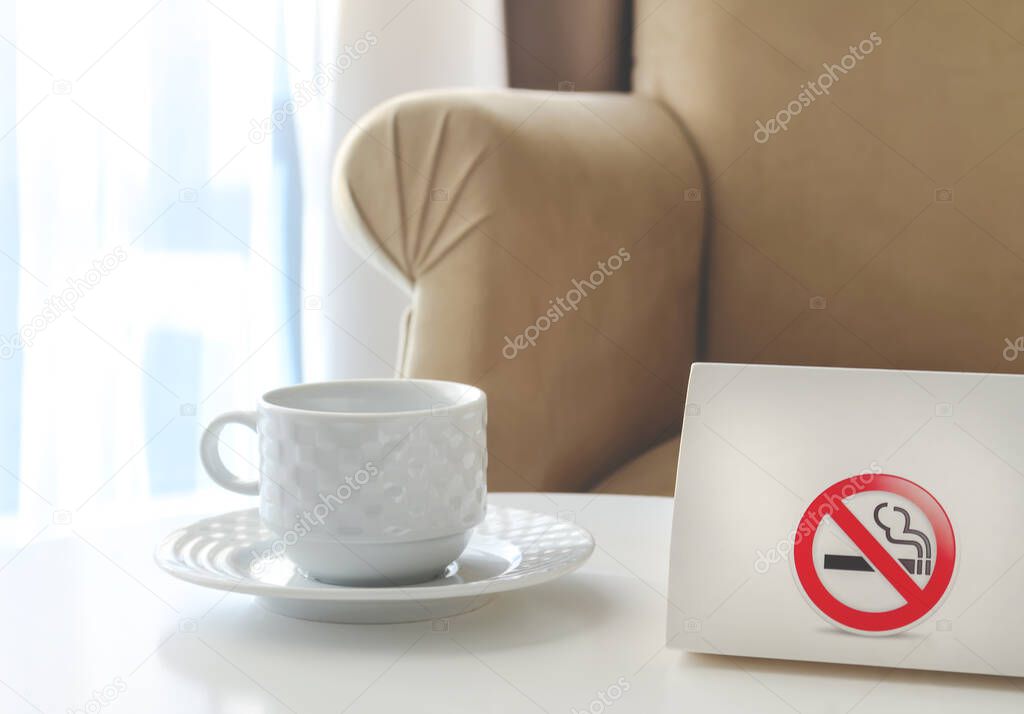 White cardboard with sign No smoking next to the tea cup on a white table.