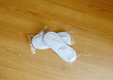 Yeni tek kullanımlık terlikler şeffaf bir pakette ahşap zeminde yatıyor.