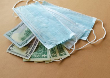 Kahverengi arka planda mavi tıbbi tek kullanımlık koruyucu maskeli Amerikan kağıt para birimi. Salgın konsepti