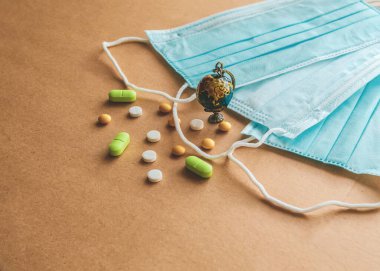Mavi tıbbi tek kullanımlık koruyucu maske, küçük küre ve kahverengi arka planda tabletler. Coronavirus konsepti