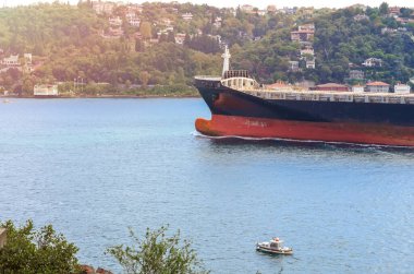 Boğazın kıyısında yelken açan büyük bir kargo gemisinin pruvası ve küçük bir tekne.