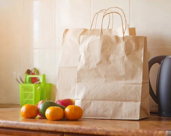 Paper bags, fresh vegetables and fruits next to a mobile phone on the table with kitchen utensils. Concept of shopping, healthy eating and vegetarianism.