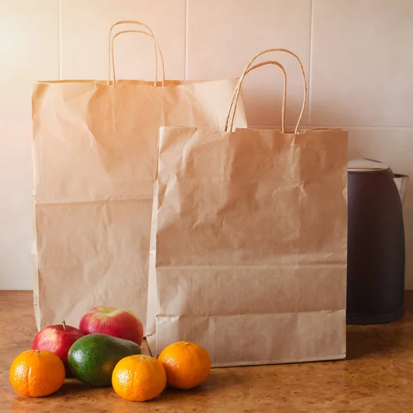 Paper bags, fresh vegetables and fruits next to a mobile phone on the table with kitchen utensils. Concept of shopping, healthy eating and vegetarianism.