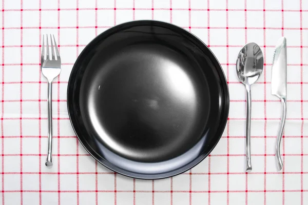 Messer schwarzer Teller und Gabellöffel auf rot karierter Tischdecke — Stockfoto