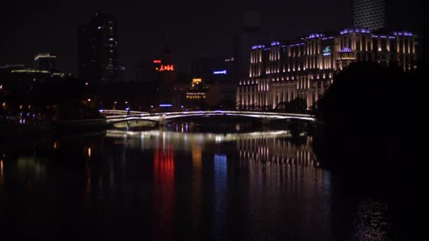 Shanghai - október 30, 2019: Fényesen Lit Bridge épületek körül tükröződik a folyó éjjel — Stock videók