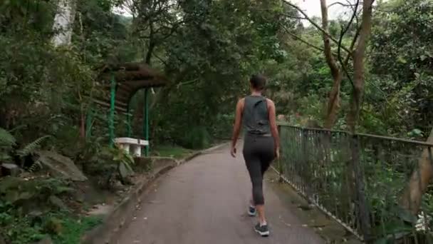 Hermosa chica en una caminata camina por el sendero de la montaña, gira y sonríe 4k — Vídeo de stock