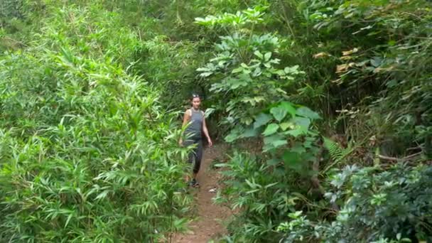 Menina mista atraente em roupas de treino Caminhadas thru Greenery Coloca em óculos de sol — Vídeo de Stock