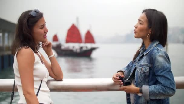 Młode kobiety rozmawiać przez molo śmiejąc się ciężko z łodzi z czerwonymi żaglami za — Wideo stockowe