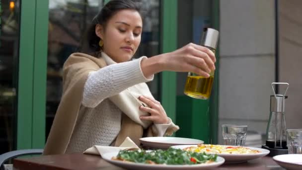 Atractiva joven mixta vierte aceite en la pizza fuera de la mesa Restaurante 4k — Vídeos de Stock