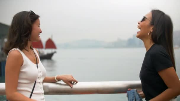 Mujeres bastante jóvenes hablan por muelle riendo duro con velas rojas barco detrás de ellos — Vídeo de stock