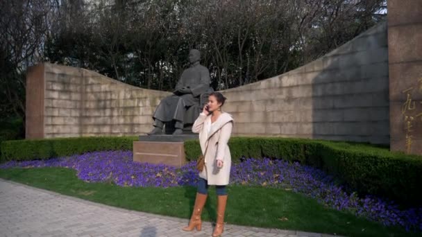 Attraktive junge Frau telefoniert im Herbst neben Denkmal — Stockvideo