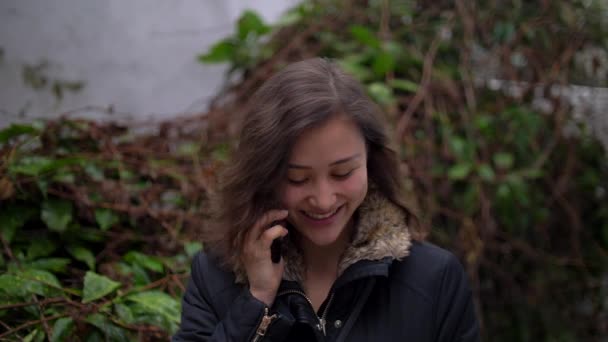 Leende ung blandad kvinna pratar på telefonen utanför med vinterjacka på 4k — Stockvideo