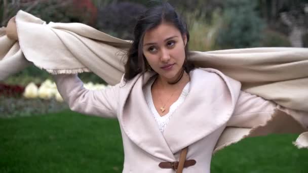 Mooie gemengde jonge vrouw zet op een sjaal op een winderige dag buiten 4k — Stockvideo