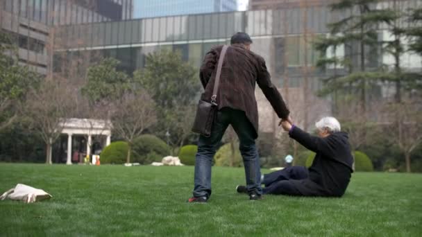 中国男人帮助一位中国老妇人从草坪上站起来 — 图库视频影像