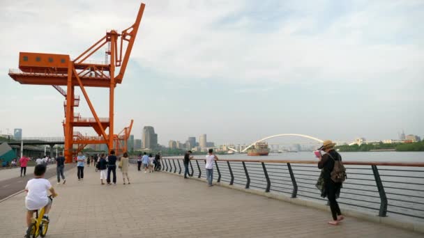 Люди гуляют вдоль реки Хуанпу со стальной конструкцией на заднем плане, день, 4k — стоковое видео