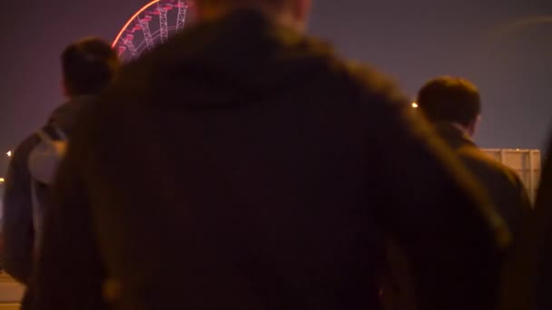 Multitud de personas cruzando la carretera hacia el parque de atracciones iluminado por la noche 4k — Vídeos de Stock