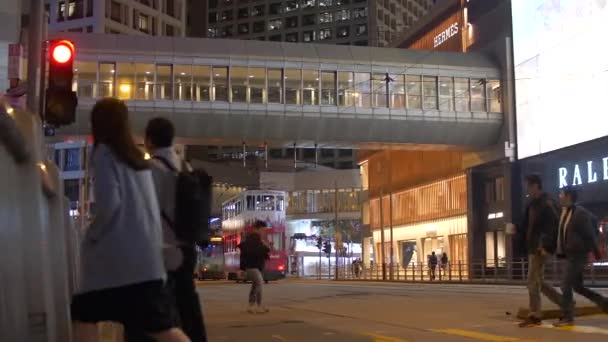 Menschen überqueren nachts in Hongkong die Straße durch Fußgängerbrücke und Straßenbahnen 4k — Stockvideo