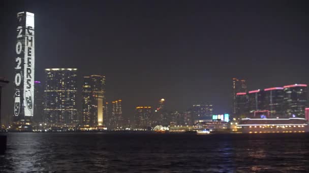 Honk Kong ICC edificio Illuminato brillantemente di notte attraverso Victoria Harbour 4k — Video Stock