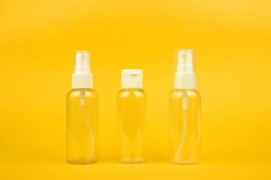 Empty cosmetic plastic bottles with pump and spray for shampoo and gel on yellow background. Clear cosmetic containers kit for travel. Template, mockup for advertising, web, social media. Stock photo.
