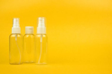 Empty cosmetic plastic bottles with pump and spray on yellow background with copy space. Clear cosmetic containers kit for travel. Template, mockup for advertising, web, social media. Stock photo.