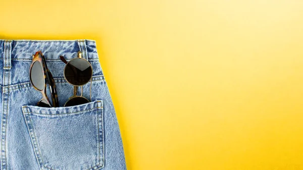 Óculos de sol no bolso de calça plana jazia no fundo amarelo. Verão, férias e férias conceito. Verão colorido roupa de moda vista superior. Modelo de banner para web, publicidade, mídia. Foto stock . — Fotografia de Stock