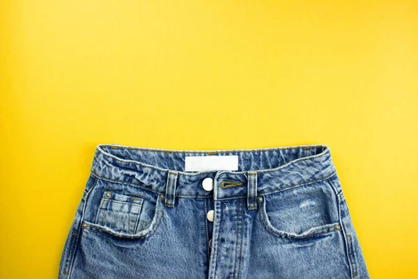 Calça jeans unissex azul com etiqueta branca plana colocada no fundo amarelo com espaço de cópia para texto, logotipo. Roupas de moda todos os dias em estilo mínimo. Modelo de banner, mockup para web, publicidade, mídias sociais . — Fotografia de Stock