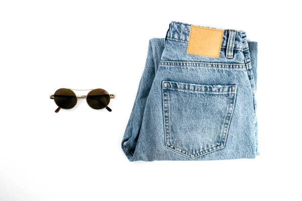 Los vaqueros unisex azules con etiqueta de cuero y gafas de sol planas yacían aislados sobre fondo blanco con espacio para copiar. Ropa de moda de estilo minimalista todos los días. Plantilla, maqueta para web, publicidad, redes sociales . —  Fotos de Stock