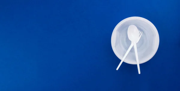 White plastic disposable tableware, utensil flat lay on trendy blue background. Contrast color. Plastic plate, bowl, spoon, fork. Top view copy space. Recycling concept. Banner template. Stock photo. — 스톡 사진