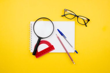Okul ve ofis malzemeleri renkli sarı arka planda duruyordu. Büyüteç, açıölçer, çizim defteri, kalem, kalem ve gözlük çizimi üst görünüm. Okul konseptine geri dönelim. Ağ şablonu. Stok fotoğrafı.