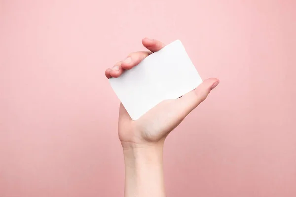 Main féminine tenant une carte de visite blanche sur fond rose coloré. Modèle, maquette, blanc pour le web, les médias sociaux, la publicité avec espace de copie. Marketing, concept technologique. Photo de stock . — Photo