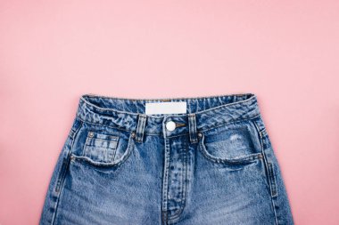 Beyaz etiketli mavi unisex kot, modaya uygun pembe arka planda, metin ve logo için fotokopi alanı ile yatıyordu. Moda kıyafetleri asgari düzeyde. Banner şablonu, sosyal medya için model. Stok fotoğrafı.