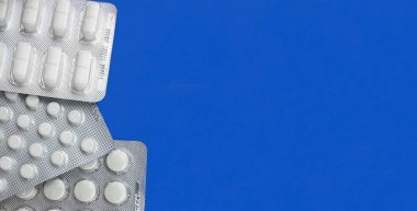 Kabarcık paketlerindeki yeni beyaz ilaç hapları yakın plan pankartı modaya uygun mavi arka plan üst görünümü üzerinde duruyor, kopyalama alanı. Hastalık, hastalık, virüs konsepti. İlaç şişiren antibiyotikler. Stok fotoğrafı