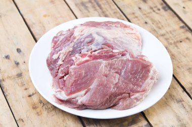 Beyaz tabak, ahşap masa üzerinde çiğ domuz eti.