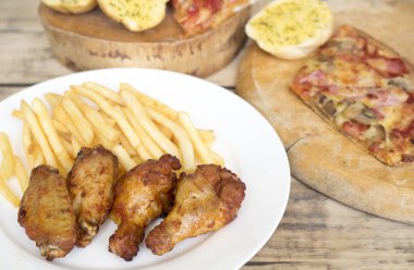 Fast food, çıtır tavuk kanatları, ekmek, patates kızartması ve pizza üzerinde 