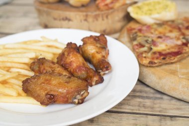 Fast food, çıtır tavuk kanatları, ekmek, patates kızartması ve pizza üzerinde 