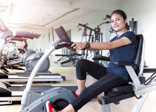 Asiatische Frau Reiten stationären Fahrrad in Turnhalle. — Stockfoto