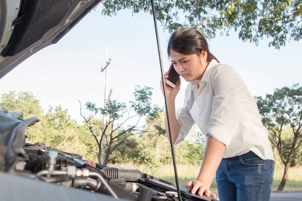 Asian young woman looking at broken down car engine on street. O — Stock Photo, Image
