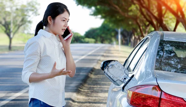 Aceite de coche abajo y mujer joven tratando de pedir ayuda por teléfono —  Fotos de Stock